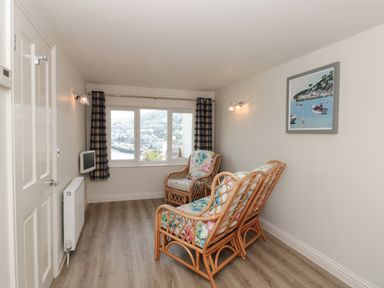 A small sitting room with two wicker armchairs and a wall-mounted television at Estuary View House & Annexe in Dartmouth