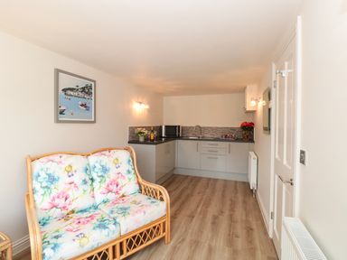 A small kitchen area with gray cabinets and a wooden floor with a floral cushioned sofa at Estuary View House and Annexe in Dartmouth
