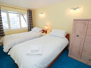 A bedroom with two single beds a bedside table with a lamp and a wooden wardrobe at Estuary View House and Annexe in Dartmouth