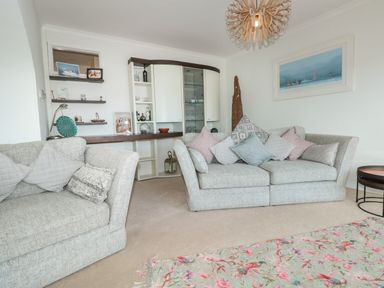 A living room with two sofas and cushions a cabinet shelves and a painting on the wall at Estuary View House and Annexe Dartmouth