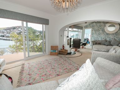 A living room with large windows overlooking water two armchairs a rug and patterned wallpaper at Estuary View House and Annexe Dartmouth