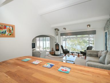 A living room with armchairs a wood stove and large windows overlooking water at Estuary View House and Annexe Dartmouth