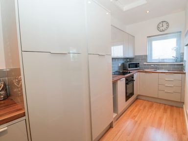 A kitchen with white cabinets wooden countertops a microwave an oven a cooktop a sink and a clock on the wall at The Snug in Beadnell