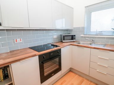 A kitchen with wooden countertops a black oven white cabinets a microwave and a stainless steel sink at The Snug in Beadnell