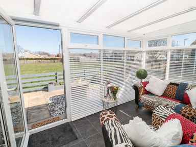A conservatory with animal print sofas white blinds and a small table with flowers at The Snug in Beadnell