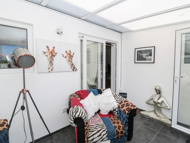 A room with a patterned armchair white pillows a tripod floor lamp giraffe and bull artwork at The Snug in Beadnell