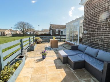 A patio with a sectional sofa and potted plants next to a brick house at The Snug in Beadnell