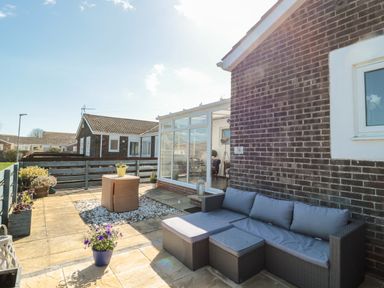 An outdoor patio area with a wicker sofa set and potted plants next to a brick house at The Snug in Beadnell