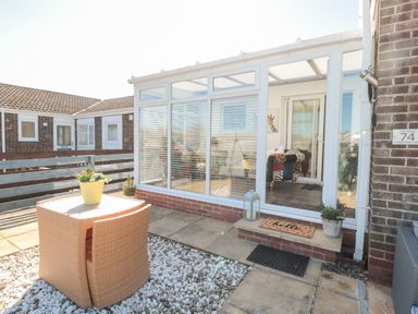 A small enclosed patio with a wicker table and chairs and potted plants at The Snug in Beadnell