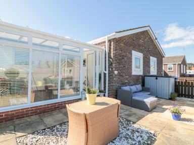 A patio area with outdoor furniture and a conservatory attached to a brick house at The Snug in Beadnell