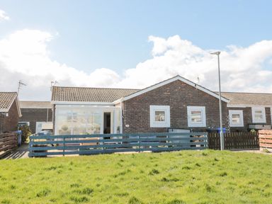 A single-story brick house with a blue fence and a grassy lawn in front at The Snug in Beadnell