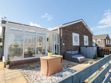 An outdoor patio area with a wicker table and chairs a gray outdoor sofa and a glass conservatory attached to a brick house at The Snug in Beadnell