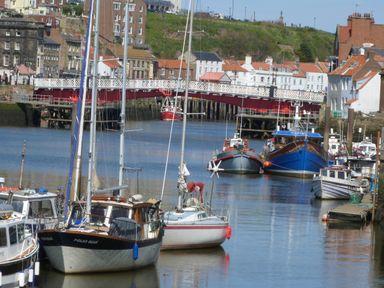 Boats docked in a harbor with a red and white bridge and buildings in the background at Stakesby House Apartment 3 Whitby