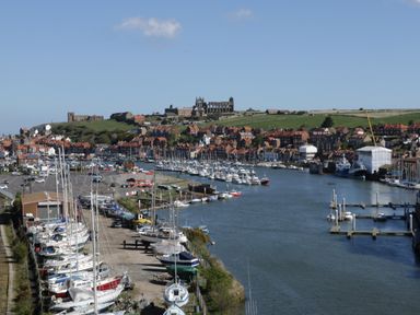 A river with boats docked on both sides and houses with red roofs on a hill at Stakesby House Apartment 3 in Whitby