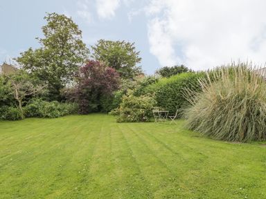 A grassy garden area with shrubs trees and a small table with two chairs at Stakesby House Apartment 3 in Whitby