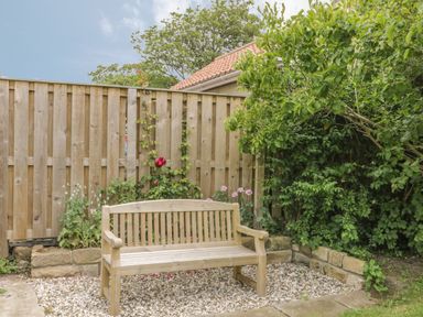 A wooden bench on gravel in a garden with a wooden fence and plants at Stakesby House Apartment 3 in Whitby
