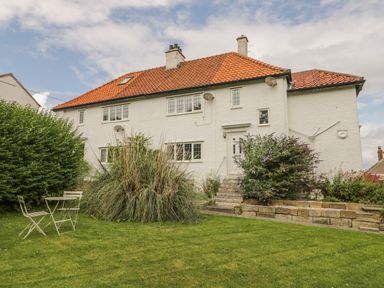 A white two-story house with a red tiled roof and garden furniture on the lawn at Stakesby House Apartment 3 in Whitby