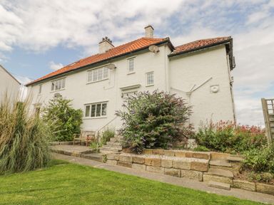 A white two-story house with a red tiled roof and garden in front at Stakesby House Apartment 3 in Whitby