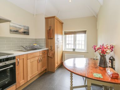 A kitchen with wooden cabinets a sink an oven a round wooden table with flowers and a window at Stakesby House Apartment 3 Whitby