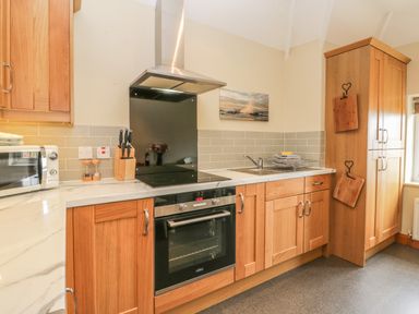 A kitchen with wooden cabinets a black oven a microwave and a sink at Stakesby House Apartment 3 Whitby