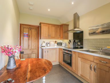 A kitchen with wooden cabinets a wooden table with flowers on it and a stainless steel oven at Stakesby House Apartment 3 in Whitby