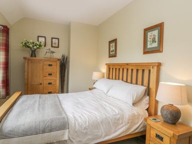 A bedroom with a wooden bed and furniture including nightstand and dresser at Stakesby House Apartment 3 Whitby