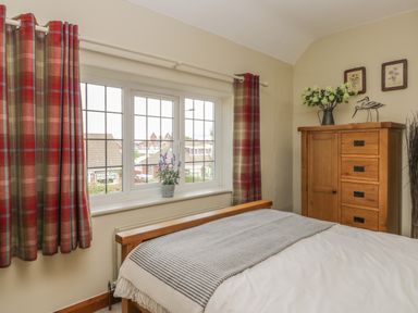 A bedroom with a wooden bed a striped blanket a wooden chest of drawers with flowers and decorative items and red plaid curtains at Stakesby House Apartment 3 Whitby