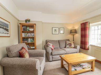 A living room with a sofa and armchair a wooden coffee table bookshelf and window with curtains at Stakesby House Apartment 3 Whitby