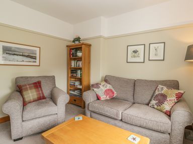 A living room with an armchair, a sofa with cushions, a wooden bookshelf, a coffee table, and framed pictures on the wall at Stakesby House Apartment 3 Whitby
