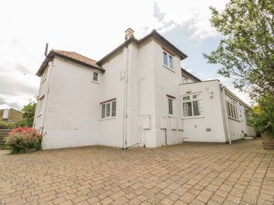 An exterior view of a white two-story house with tiled roof and paved driveway with some plants on the sides at Stakesby House Apartment 3 Whitby