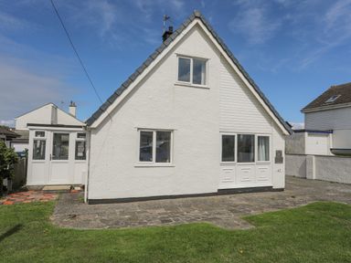 A front view of a white detached house with windows a door and a driveway with grass at Crows Nest - Rhosneigr in Rhosneigr
