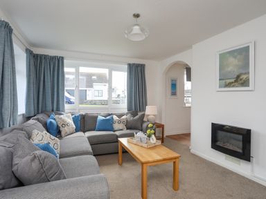 A living room with a gray sectional sofa and blue curtains at Crows Nest - Rhosneigr