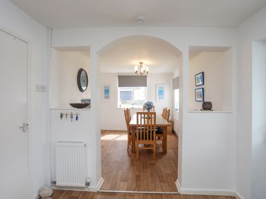 A dining room with a wooden table and chairs under a chandelier at Crows Nest - Rhosneigr in Rhosneigr