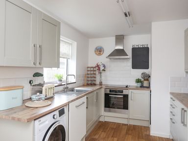 A kitchen with wooden countertops a washing machine a toaster and an oven at Crows Nest - Rhosneigr in Rhosneigr
