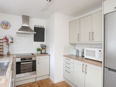 A kitchen with a stainless steel oven and hood a microwave and storage cabinets at Crows Nest - Rhosneigr in Rhosneigr