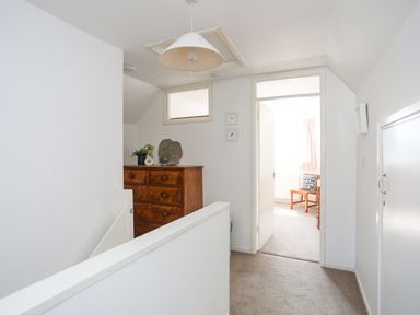 A hallway with a wooden chest of drawers and a chair visible in an adjacent room at Crows Nest - Rhosneigr in Rhosneigr