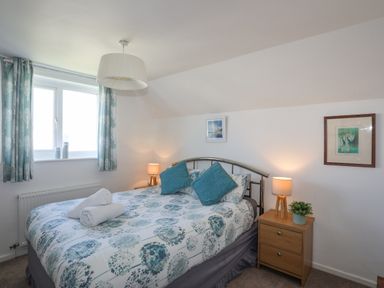 A bedroom with a double bed two bedside tables with lamps and framed pictures on the wall at Crows Nest - Rhosneigr in Rhosneigr