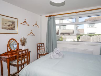 A bedroom with a wooden dressing table and chairs with a large window and a bed at Crows Nest - Rhosneigr in Rhosneigr