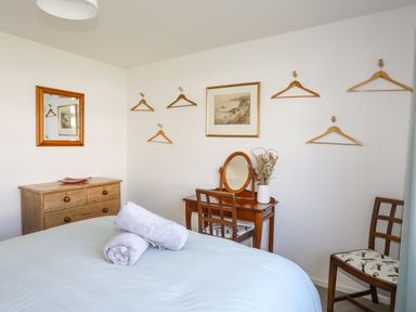 A bedroom with a bed and towels on it a dresser with a mirror and a dressing table with a chair at Crows Nest - Rhosneigr in Rhosneigr