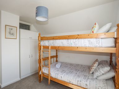 A bedroom with a wooden bunk bed and a white wardrobe at Crows Nest - Rhosneigr in Rhosneigr