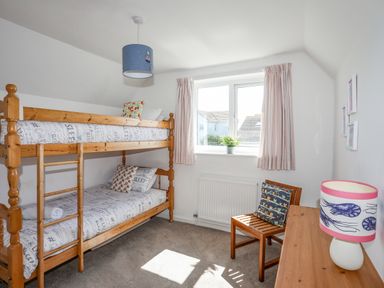 A bedroom with wooden bunk beds a window with curtains a wooden chair and a desk with a lamp at Crows Nest - Rhosneigr in Rhosneigr