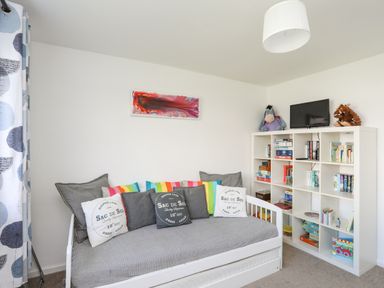 A small room with a daybed with cushions and a white shelving unit with books and toys at Crows Nest - Rhosneigr in Rhosneigr