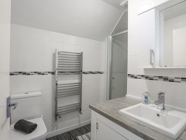 A bathroom with a toilet a towel rack a sink with a faucet and a mirror cabinet at Crows Nest - Rhosneigr in Rhosneigr