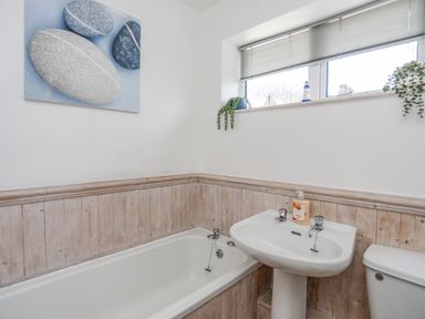 A bathroom with a bathtub sink and toilet with a window above and a painting of stones on the wall at Crows Nest - Rhosneigr in Rhosneigr