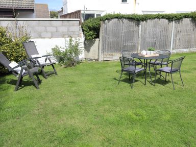 A garden with two reclining chairs and a round table with four chairs at Crows Nest - Rhosneigr in Rhosneigr