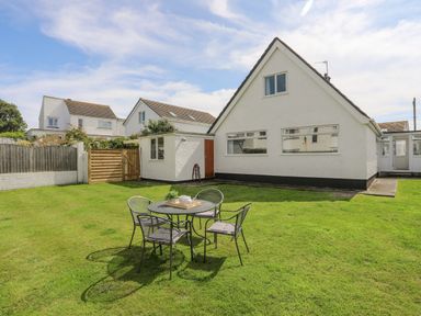 A backyard with a round table and four chairs on grass outside a white house at Crows Nest - Rhosneigr in Rhosneigr