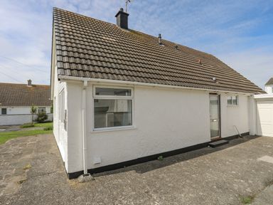 A white house with a tiled roof and paved driveway at Crows Nest Rhosneigr