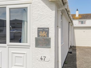 The exterior corner of a white house with plaques displaying The Crows Nest and the number 47 in Rhosneigr