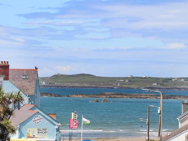 A coastal scene with a surf shop building flags on poles and a view of the sea with distant hills at Crows Nest - Rhosneigr in Rhosneigr