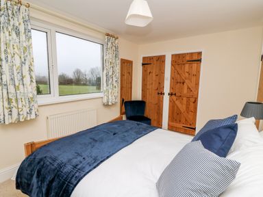 A bedroom with a bed, blue cushions, floral curtains, a window, wooden doors, and a blue chair at Gwynfa in Capel Iwan near Newcastle Emlyn